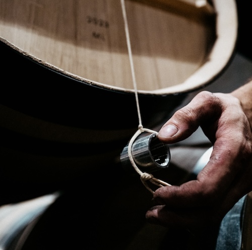 Close up of hand steadying hanging weight for aligning wine barrels.