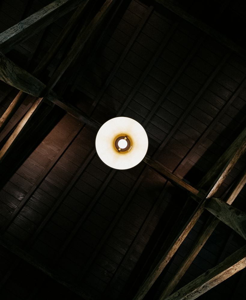 The wooden beams of the ceiling of the winery at Brane-Cantenac, showing a hanging lamp in the middle.
